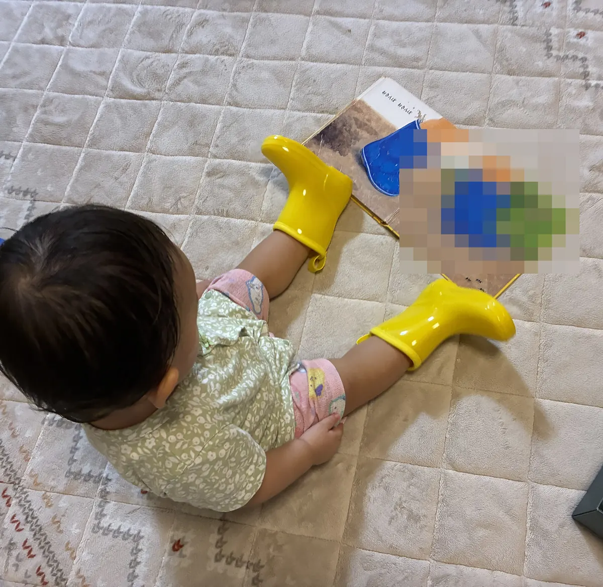 黄色い長ぐつを履いて、長ぐつが出てくる絵本を見る1歳の娘